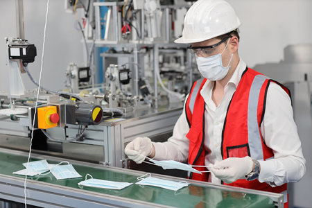 Caucasian mechanic technician maintenance or PPE inspecting quality of mask and medical face mask production line in factory, manufacturing industry and factory concept.の写真素材