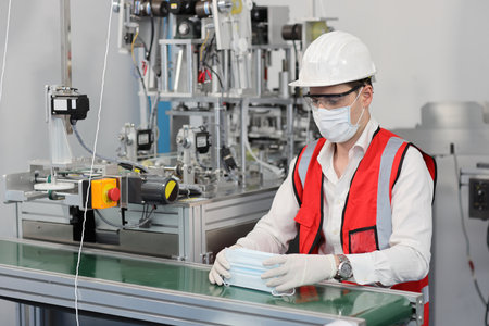 Caucasian mechanic technician maintenance or PPE inspecting quality of mask and medical face mask production line in factory, manufacturing industry and factory concept.の写真素材