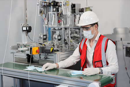 Caucasian mechanic technician maintenance or PPE inspecting quality of mask and medical face mask production line in factory, manufacturing industry and factory concept.の写真素材