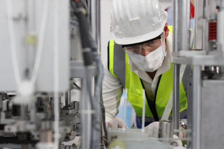 Caucasian mechanic technician maintenance, repairing industrial machinery equipment in factory. Professional worker in protective clothing with goggles and mask using wrench at manufacturing factoryの写真素材