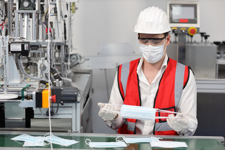 Caucasian mechanic technician maintenance or PPE inspecting quality of mask and medical face mask production line in factory, manufacturing industry and factory concept.の写真素材