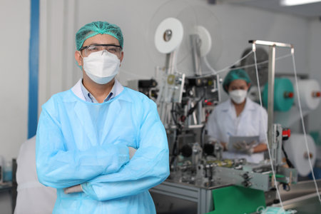 Worker in personal protective equipment or PPE inspection quality crossed arms and looking camera in mask and medical face mask production line factory, manufacturing industry and factory concept.の写真素材