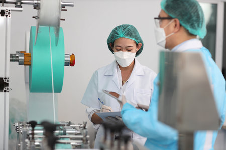 Inspector woman and colleague man working on quality of mask and medical face mask production line, Industry and factory concept.の写真素材