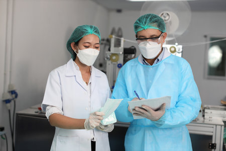 Worker man and woman in personal protective equipment or PPE inspecting checking quality of mask and medical face mask production line in factory, manufacturing industry and factory concept.の写真素材