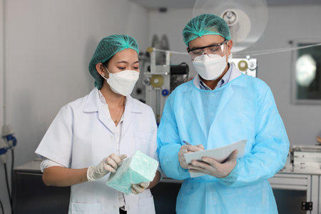 Inspector man and colleague woman working on quality of mask and medical face mask production line, Industry and factory concept.の写真素材