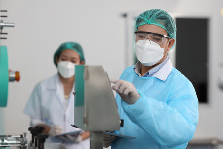 Inspector man and colleague woman working on quality of mask and medical face mask production line, Industry and factory concept.の写真素材