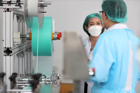 Inspector woman and colleague man working on quality of mask and medical face mask production line, Industry and factory concept.の写真素材