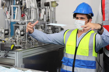 Caucasian mechanic technician maintenance or PPE inspecting quality of mask and medical face mask production line in factory, manufacturing industry and factory concept.の写真素材