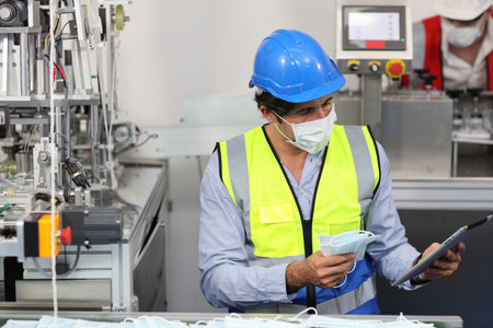 Caucasian mechanic technician maintenance or PPE inspecting quality of mask and medical face mask production line in with tablet factory, manufacturing industry and factory concept.の写真素材