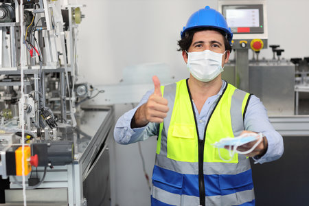 Caucasian mechanic technician maintenance or PPE inspecting quality of mask and medical face mask production line in factory while showing thumb up, manufacturing industry and factory concept.の写真素材