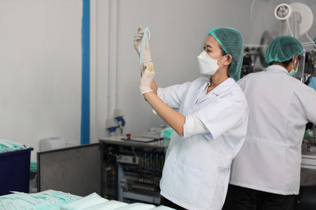 Worker woman in personal protective equipment or PPE inspecting quality of mask and medical face mask production line in factory, manufacturing industry and factory concept.の写真素材