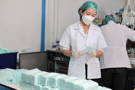 Worker woman in personal protective equipment or PPE inspecting showing quality of mask and medical face mask production line in factory, manufacturing industry and factory concept.の写真素材