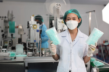 Worker woman in personal protective equipment or PPE inspecting showing quality of mask and medical face mask production line in factory, manufacturing industry and factory concept.の写真素材