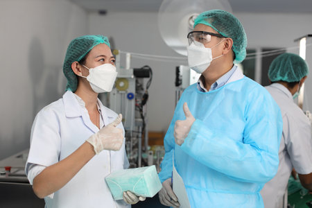 Inspector man and colleague woman working on quality of mask and medical face mask production line while showing thumb up at Industry and factory.の写真素材
