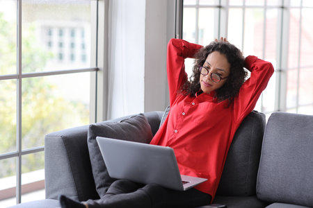 Happy woman sitting and using computer and raising hands with happy smiling face while completed business deal in living room. Businesswoman raising hands and exciting emotion with somthing successfulの写真素材