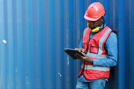 Foreman using tablet and walkie talkie radio control loading containers box. Engineer or worker with safety hat work at container cargo site and checking industrial container cargo freight ship.の写真素材