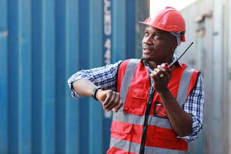 Foreman engineer using walkie talkie radio control loading containers box. Confident engineering with helmet work at container cargo site and checking industrial container cargo freight shipの写真素材