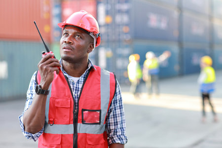 Foreman engineer using walkie talkie radio control loading containers box. Confident engineering with helmet work at container cargo site and checking industrial container cargo freight shipの写真素材