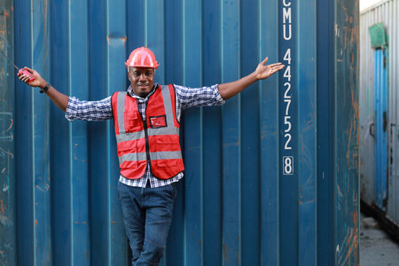 Happy smiling foreman engineer or working in protective uniform with hardhat raising hands meaning of celebrate successful completed deal commitment at industrial container cargo freight shipの写真素材