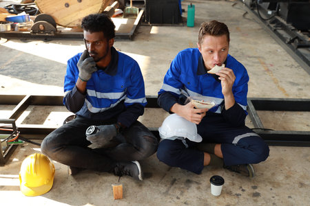 Happy teamwork technician engineer in safety workwear having lunch and eating sandwich and coffee at industry manufacturing factoryの写真素材