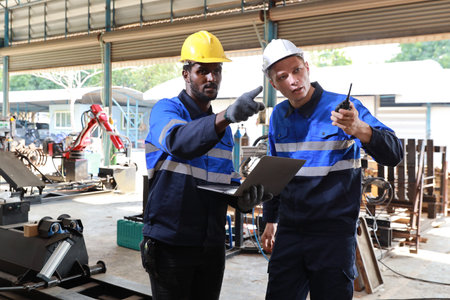 Industry technician engineer maintenance and check part of robot arm machine in intelligent factory with computer and walkie talkie while pointing. Industrial and technology support system conceptの写真素材