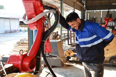 Technician engineer worker man in safety uniform suffering from backache or having problem with body from work accident at industrial robotic factory. First aid, healthy or insurance at work conceptの写真素材