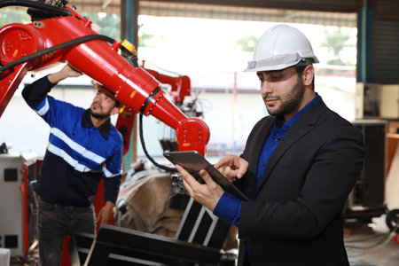 Professional heavy industry technician engineer in safety workwear and businessman maintenance and check part of robot arm machine with tablet in factory automotive. Industrial and technology conceptの写真素材