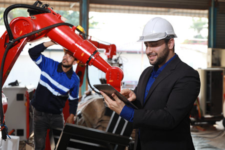 Professional heavy industry technician engineer in safety workwear and businessman maintenance and check part of robot arm machine with tablet in factory automotive. Industrial and technology conceptの写真素材