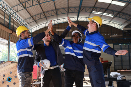 Group of technician engineer and businessman in protective uniform with hardhat standing and raising hands celebrate successful together or completed deal commitment at metal lathe factory industryの写真素材