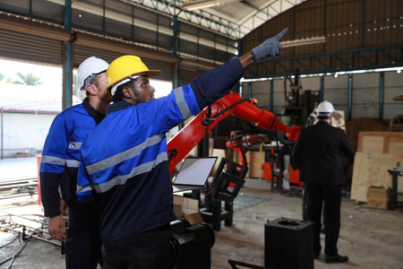 Professional heavy industry technician engineer maintenance and check part of robot arm machine in intelligent factory with computer and walkie talkie. Industrial and technology support system conceptの写真素材
