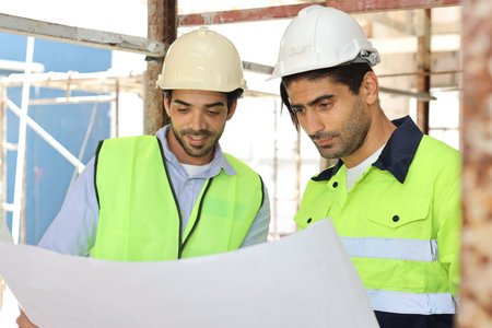 Two technician civil engineer or specialist inspector discussing, brainstorm and planing work with laptop, blueprint and walkie talkie radio together at Industrial building site. Construction conceptの写真素材