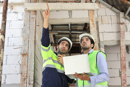 Two technician civil engineer or specialist inspector pointing, discussing and plan work with laptop, blueprint and walkie talkie radio together with at Industrial building site. Construction conceptの写真素材