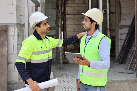 Two technician civil engineer or specialist inspector discussing, brainstorm and planing work with laptop, blueprint and walkie talkie radio together at Industrial building site. Construction conceptの写真素材