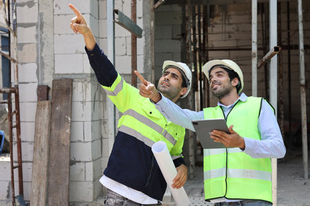 Two technician civil engineer or specialist inspector pointing, discussing and plan work with tablet, blueprint and walkie talkie radio together with at Industrial building site. Construction conceptの写真素材
