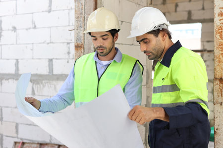 Two technician civil engineer or specialist inspector discussing, brainstorm and planing work with laptop, blueprint and walkie talkie radio together at Industrial building site. Construction conceptの写真素材