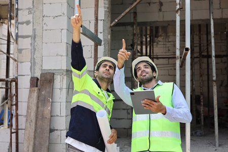 Two technician civil engineer or specialist inspector pointing, discussing and plan work with tablet, blueprint and walkie talkie radio together with at Industrial building site. Construction conceptの写真素材