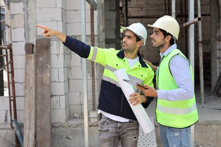 Two technician civil engineer or specialist inspector pointing, discussing and plan work with laptop, blueprint and walkie talkie radio together with at Industrial building site. Construction conceptの写真素材