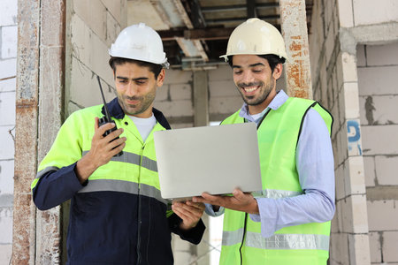 Two technician civil engineer or specialist inspector discussing, brainstorm and planing work with laptop, blueprint and walkie talkie radio together at Industrial building site. Construction conceptの写真素材