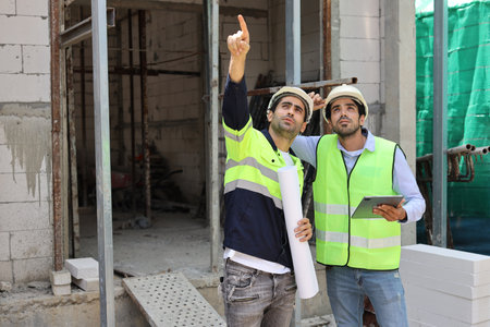 Two technician civil engineer or specialist inspector pointing, discussing and plan work with tablet, blueprint and walkie talkie radio together with at Industrial building site. Construction conceptの写真素材