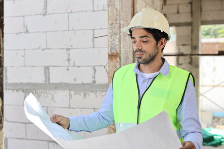 Caucasian technician civil engineer man or specialist inspector standing and planing real estate project work with blueprint while checking at Industrial building site. Construction conceptの写真素材