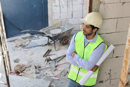 Caucasian technician civil engineer or specialist inspector standing and crossed arms while holding blueprint and looking away after project complete at Industrial building site. Construction conceptの写真素材