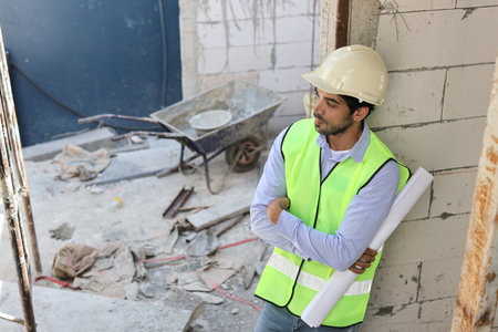 Caucasian technician civil engineer or specialist inspector standing and crossed arms while holding blueprint and looking away after project complete at Industrial building site. Construction conceptの写真素材
