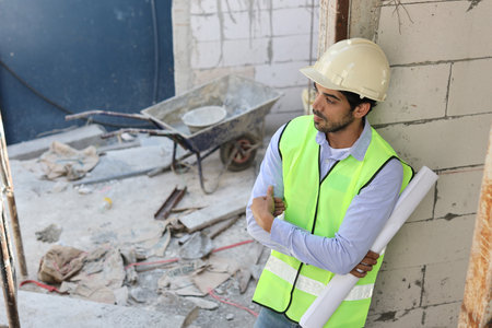 Caucasian technician civil engineer or specialist inspector standing and crossed arms while holding blueprint and looking away after project complete at Industrial building site. Construction conceptの写真素材