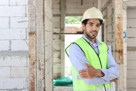 Caucasian technician civil engineer or specialist inspector standing and crossed arms while looking at camera with happy face after project complete at Industrial building site. Construction conceptの写真素材