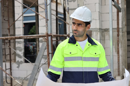 Caucasian technician civil engineer man or specialist inspector standing and planing real estate project work with blueprint while checking at Industrial building site. Construction conceptの写真素材