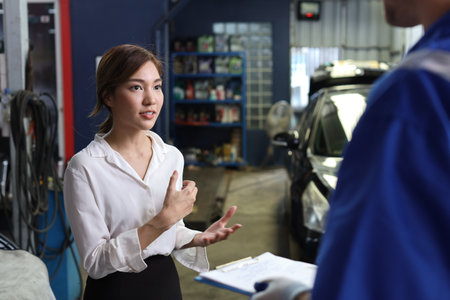 Man technician car mechanical in uniform showing car maintenance service report on clipboard at repair garage station. Auto mechanic give customer discussion on her vehicle repairs problemsÂ conditionの写真素材