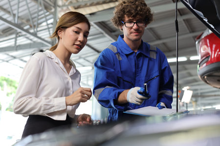 Man technician car mechanical in uniform showing car maintenance service report on clipboard at repair garage station. Auto mechanic give customer discussion on her vehicle repairs problemsÂ conditionの写真素材