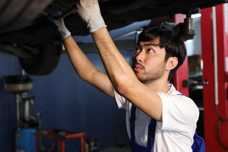 Man technician car mechanic in uniform checking or maintenance a lifted car service at repair garage station. Worker holding wrench and fixing breakdown vehicle. Concept of car center repair service.の写真素材