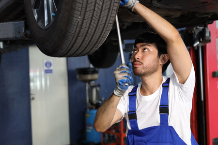 Man technician car mechanic in uniform checking or maintenance a lifted car service at repair garage station. Worker holding wrench and fixing brake discs. Concept of car center repair service.の写真素材