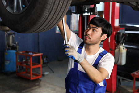 Man technician car mechanic in uniform checking or maintenance a lifted car service at repair garage station. Worker holding wrench and fixing brake discs. Concept of car center repair service.の写真素材
